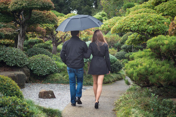 Young romantic couple walking together in park with umbrella