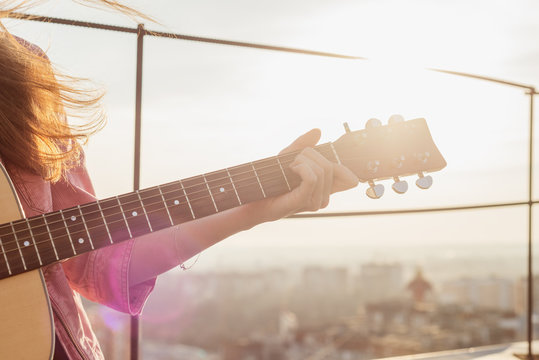 young beautiful woman play on guitar on the roof close up