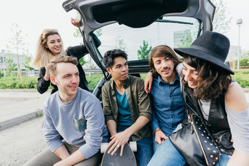 Group of friends multiethnic millennials sitting automobile boot having fun - happiness,...