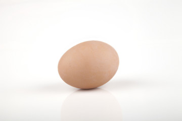 A brown egg on a white surface. Isolated on white background.