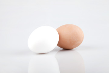 A white egg and a brown egg on a white surface. Isolated on white background.