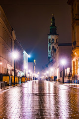 Fototapeta premium Night street in the Krakow, Poland. Colorful night illumination reflecting in the wet stone pavement of the old town. Beautiful background photo.