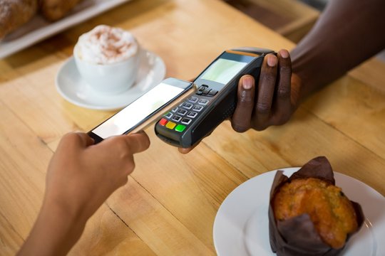 Barista accepting payment through mobile phone at cafe