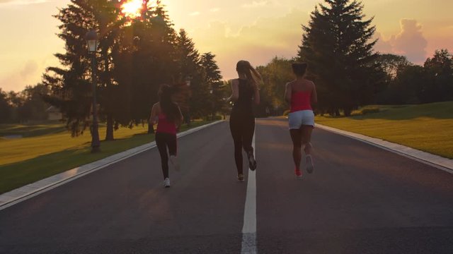 Group of women running at sunset. Back view of three fitness women running in park at sunset. Weight loss training at evening. Sporty women fitness workout outdoor. Sport women running group
