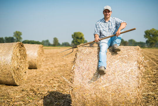 Smiling farmer sitting on an hay bale in his field