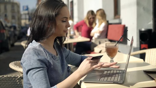 Young woman doing online shopping on laptop sitting in cafe in city

