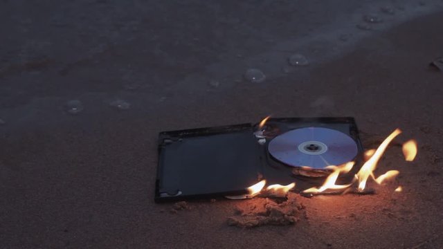 data cd dvd laser compact disc case on fire on the wet sand at coast HD