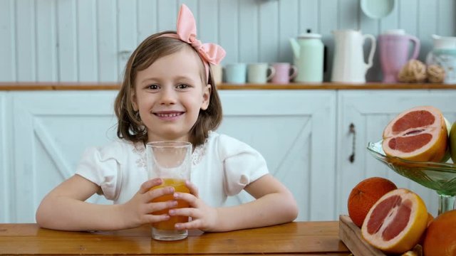 Adorable little girl drinking orange juice on breakfast on morning, small child drink, fruits on table