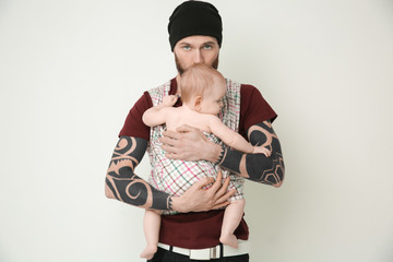 Handsome tattooed young man holding cute little baby on light background