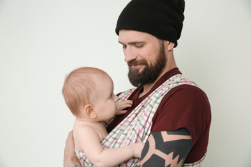Handsome tattooed young man holding cute little baby on light background
