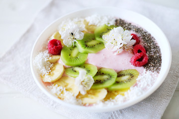 Raspberry and banana smoothie bowl with kiwi slices, shredded coconut and chia seeds.