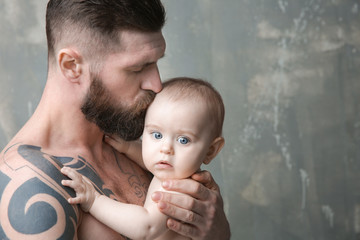 Handsome tattooed young man holding cute little baby on gray background