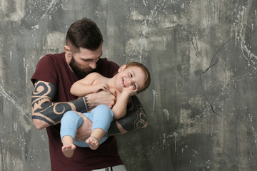 Handsome tattooed young man holding cute little boy on gray background