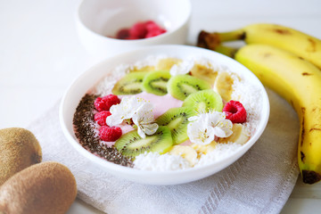 Raspberry and banana smoothie bowl with kiwi slices, shredded coconut and chia seeds.