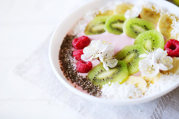 Raspberry and banana smoothie bowl with kiwi slices, shredded coconut and chia seeds.