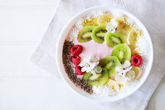 Raspberry and banana smoothie bowl with kiwi slices, shredded coconut and chia seeds.