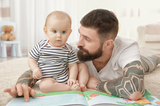 Handsome tattooed young man playing with cute little baby at home