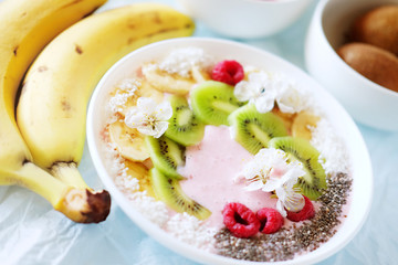 Raspberry and banana smoothie bowl with kiwi slices, shredded coconut and chia seeds.