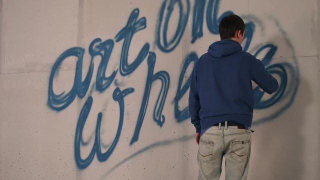 Young man drawing graffiti on a wall with a spray can
