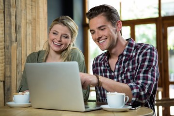 Cheerful couple using laptop at table in coffee shop