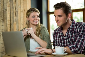 Woman looking at man using laptop in coffee shop