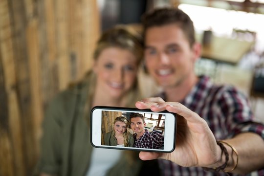 Smiling couple taking selfie with cellphone in cafeteria