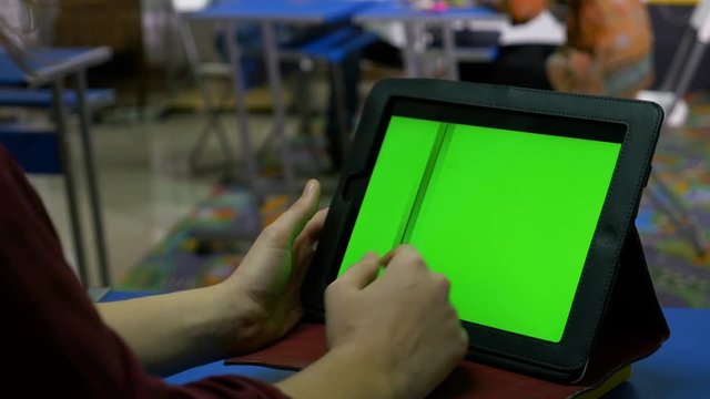 Female hands touching the green screen of a tablet pc on a desk