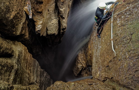 Explore the breathtaking Mayei Cave in Ecuadorian Amazonia with a speleologist inside a deep waterfall entrance shaft,capturing the blurred motion of adventure.