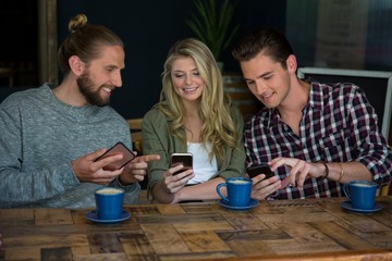 Smiling friends using smart phones at table in cafe