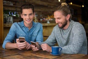 Smiling male hipsters using smart phones at table in coffee shop