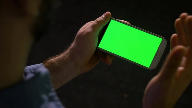 Guy holding showing and pointing at smart phone with green screen in hands