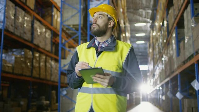Surveyor Wearing Hard Hat Holds Tablet Computer Counts Merchandise in Warehouse. He Walks Through Rows of Rack Pallets Shot on RED EPIC-W 8K Helium Cinema Camera.