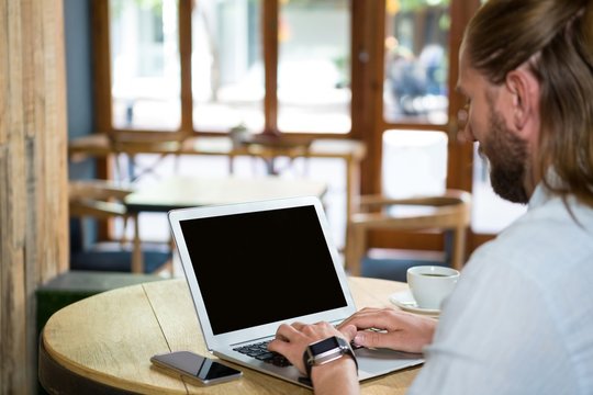 Side view of man using laptop in coffee shop