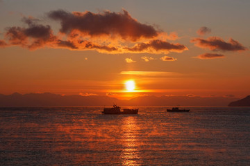 Fototapeta na wymiar Two ships floating on background of red sunset
