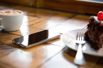 Smart phone with pastry and coffee cup on table