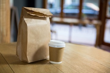 Disposable coffee cup and paper bag on table in cafe