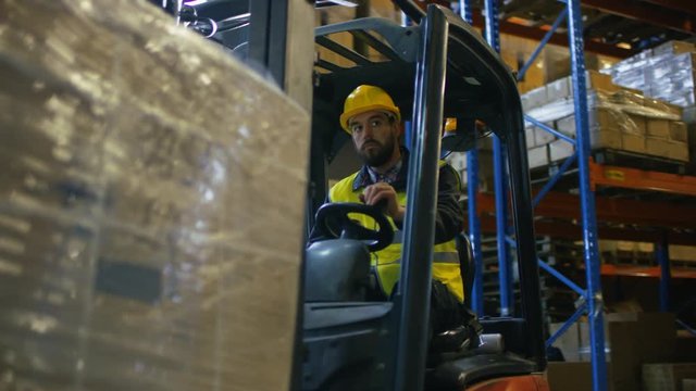 Close-up Shot of a Forklift Driver Operating Vehicle in a Big Warehouse full of Pallet Rack. Shot on RED EPIC-W 8K Helium Cinema Camera.