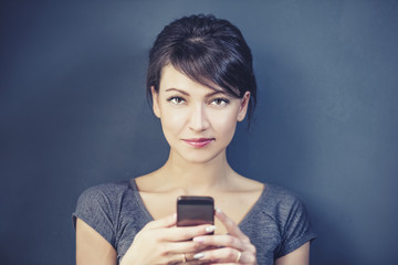 Portrait of young emotional woman on grey background with smartphone