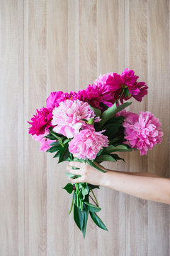 white caucasian woman holding red and pink peonies bouquet at wood wall backdrop