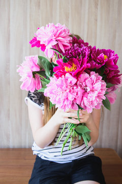 happy white caucasian girl holding red and pink peonies bouquet in front of face at wood wall backdrop
