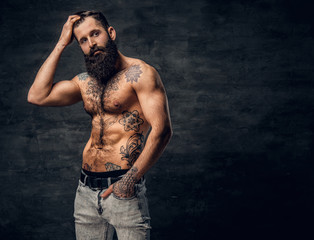 Bearded male with tattooed torso posing over dark grey background.