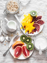 Breakfast table. Variety of fruits - mango, kiwi, grapefruit, orange and greek yogurt, oat flakes on a light background, top view. Flat lay