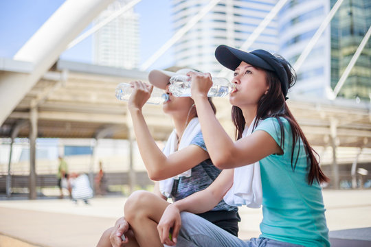 Beautiful young asian woman drinking water after training in city