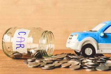 Coins spilling out of a glass jar with car label and car toy on wooden table. Financial Concept