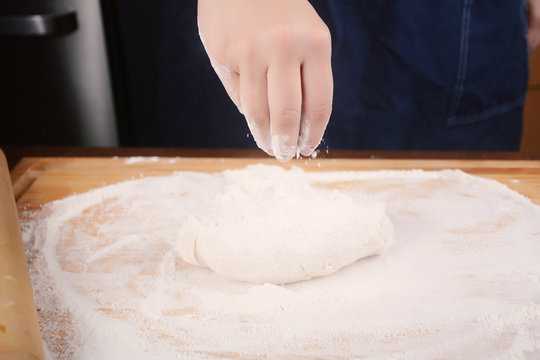 Woman hand adding flour to dough.