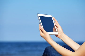Close up picture of female hands with tablet computer on a beach, blank screen with copy space.