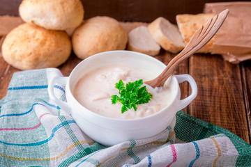 Cream soup in white bowl with wood spoon near bread on wooden background. Rustic style