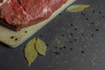 Raw beef meat with spices on wooden cutting board and dark background, top view