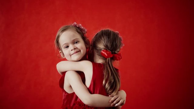 Two little girls hugging on a red background