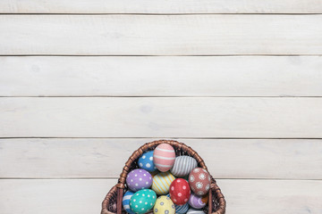 Basket with colorful Easter eggs, painted in handmade on an old white wooden background. Top view, flat lay style